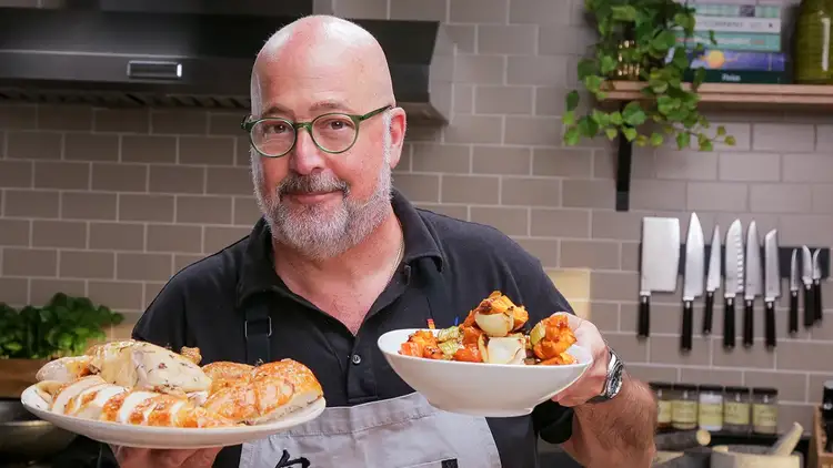 Chef Andrew Zimmern holding Roasted Chicken on a plate with Pan Gravy and vegetables in a bowl