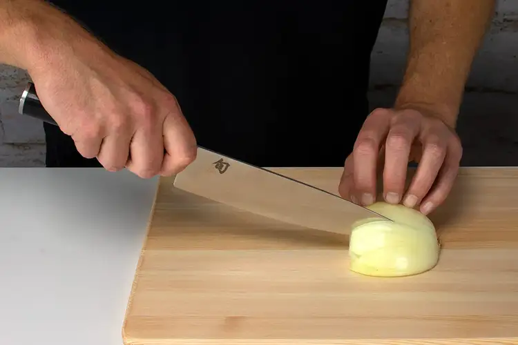 Chef using a Shun knife to slice vertically into the onion, creating layers for an even dice.