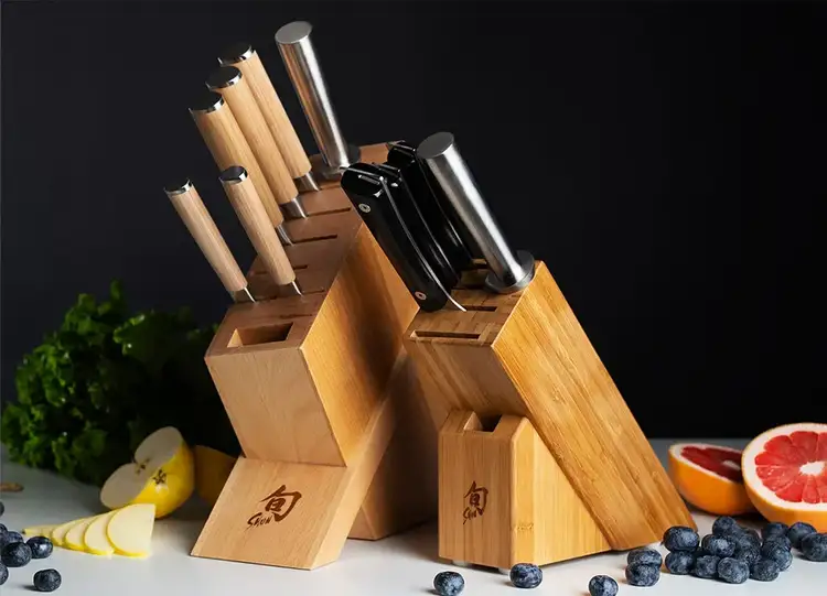 Two Shun knife block sets sit on a counter, surrounded by sliced fruits and berries.