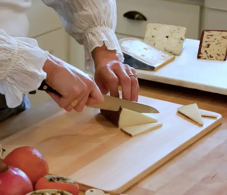 Cutting wedges from a Manchego-style cheese using a Shun knife on a wooden board.