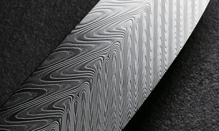 Close-up of a Shun Dual Core santoku blade highlighting the layered Damascus pattern and thin cutting edge.