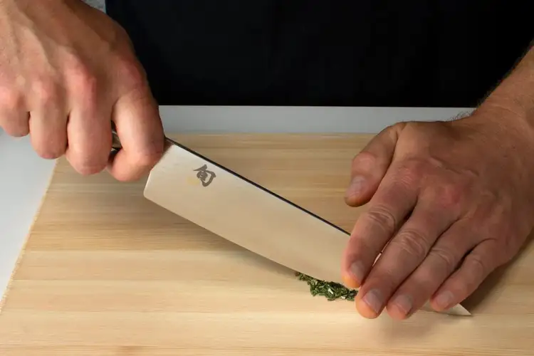 Chef using a two-handed technique to mince herbs finely with a Shun knife, stabilizing the blade with fingertips.