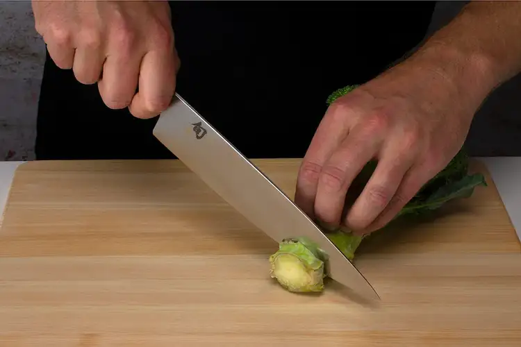 A Shun Classic Chef’s Knife cuts into the thick stalk of a head of broccoli