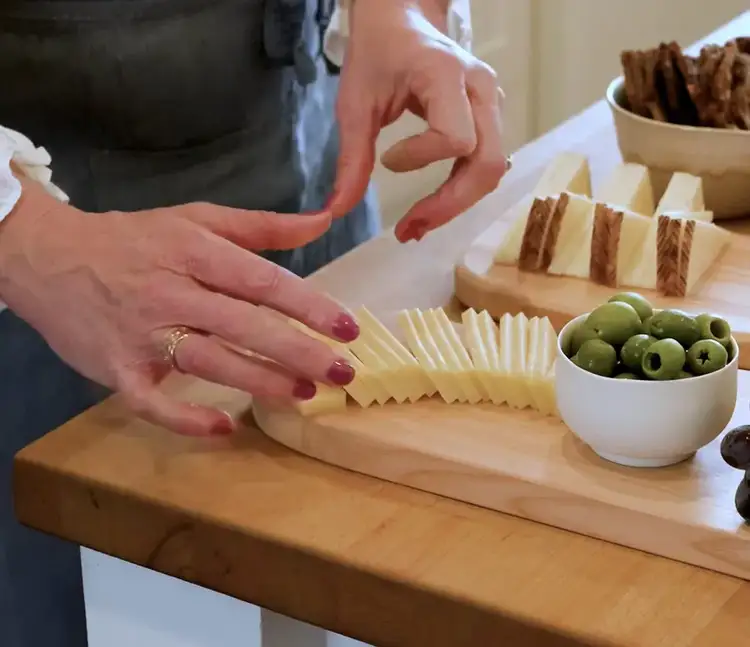 Fanning sliced Alpine cheese into a zigzag pattern next to green olives on the cheeseboard.